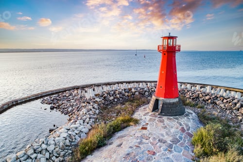 Preview: Red lighthouse on rocky harbor at sunset