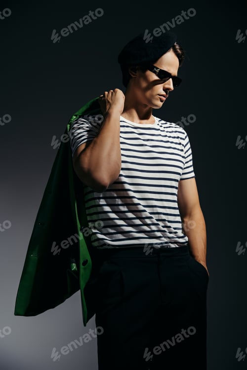 Preview: Trendy man in striped t-shirt holding green leather jacket on grey background with lighting