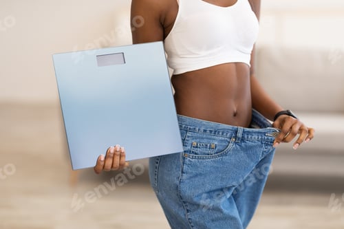 Preview: Slim Woman Holding Scales Wearing Large Jeans After Slimming Indoors
