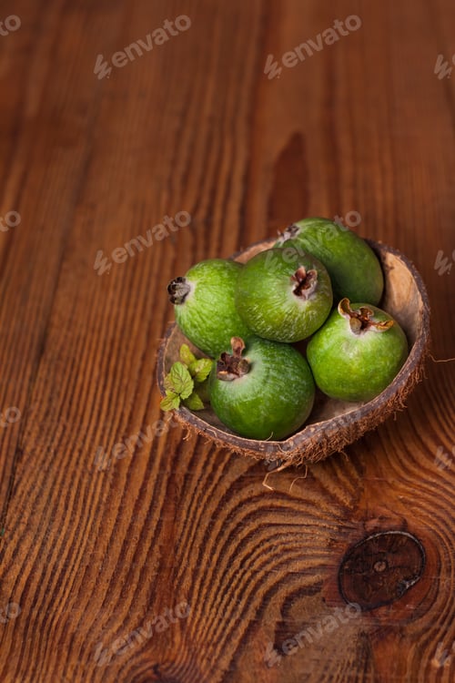 Preview: Green feijoa in coconut shell hulf wooden background. Ripe tropical fruits raw vegan foodVitamin C