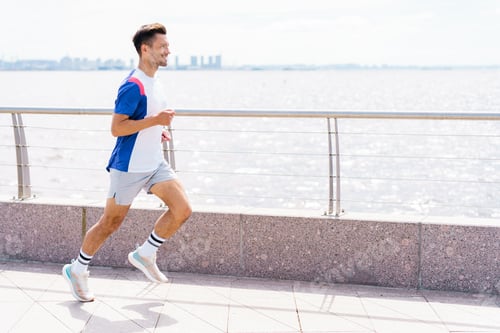 Preview: Man runner jogging along a waterfront promenade on a bright, sunny day.