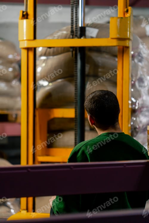 Preview: a worker at a coffee factory uses a yellow forklift to lift and place a pallet on shelf