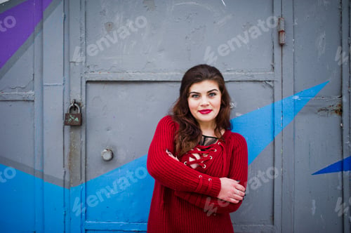 Preview: Brunette plus size model at red against colored wall.
