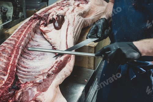 Preview: Close up of butcher wearing black rubber gloves working on a pig carcass on butcher's block,