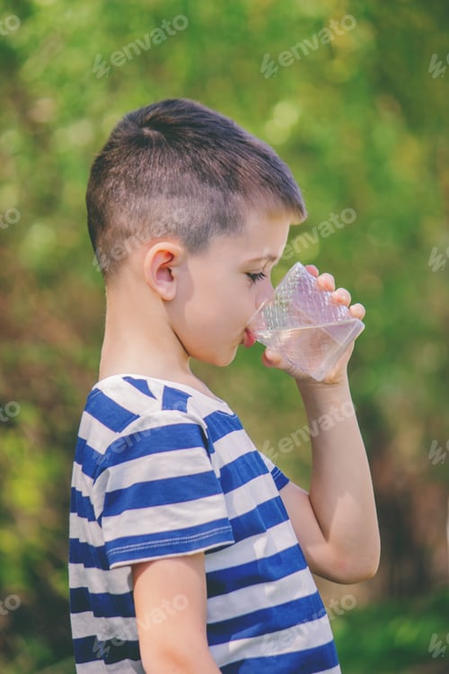 Preview: Boy drinks water from a glass on a nature background.water.