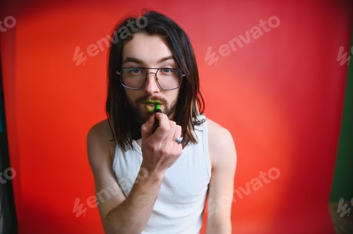 Preview: Young man applying lip gloss on his lips and looking in camera like mirror.