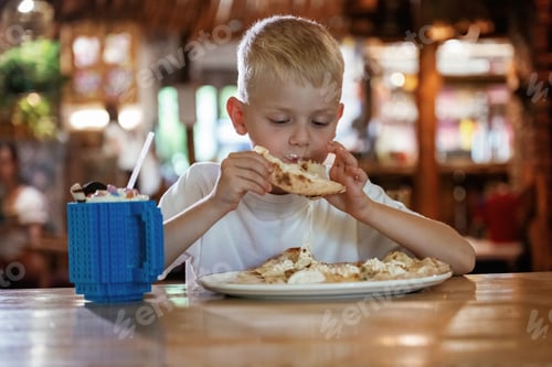 Visualização: Garotinho está sentado dentro de casa e comendo pizza deliciosa