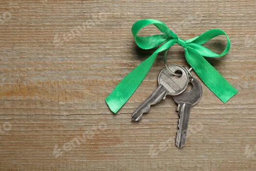 Preview: Keys with green bow on wooden table, top view and space for text. Housewarming party