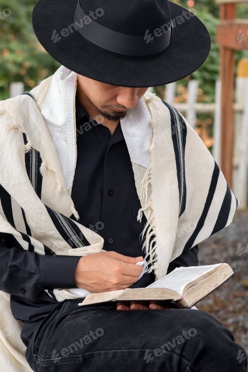 Preview: Latin Jew wearing tallit and Jewish hat sitting reading scripture in the quiet of his courtyard.