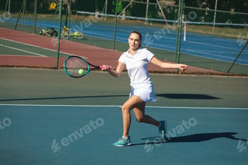 Preview: Young female caucasian athlete playing tennis with racket while hitting ball at court on sunny day