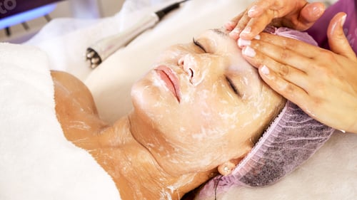 Preview: Cosmetologist applies a moisturizing mask on female face. Woman in a spa salon, cosmetic procedures