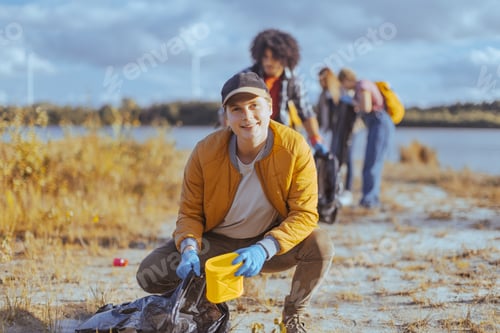 Preview: Volunteer collecting trash near river bank with group in background
