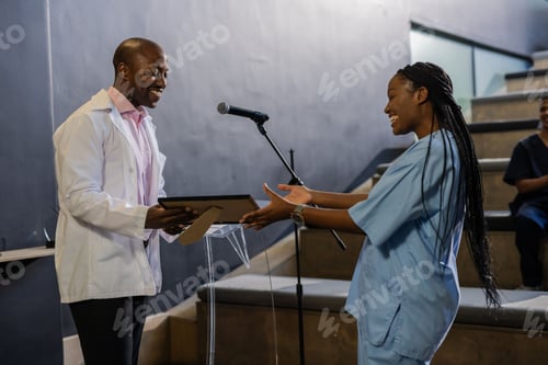 Preview: African American woman in scrubs receiving award from smiling man in white coat
