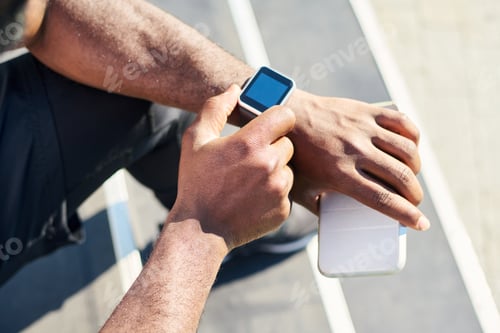 Preview: Hands of young black man sitting on staircase and checking time on wristwatch