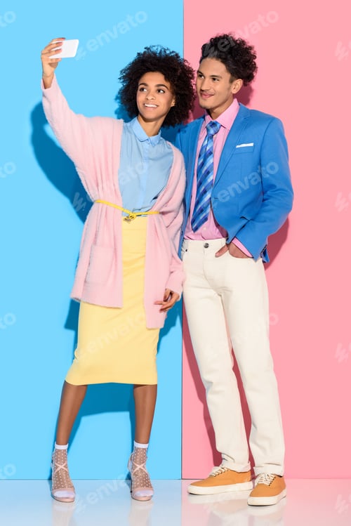 Preview: Young african amercian girl taking selfie and hugging stylish guy on pink and blue background