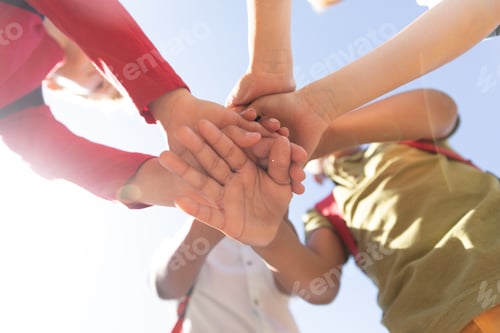 Preview: Directly below shot of multiracial elementary schoolboys stacking hands while standing against sky