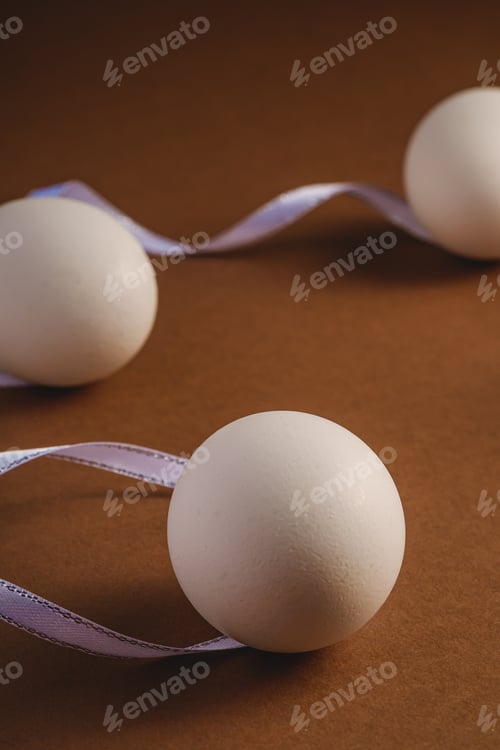 Preview: White eggs with fabric ribbon on brown paper background, happy Easter day