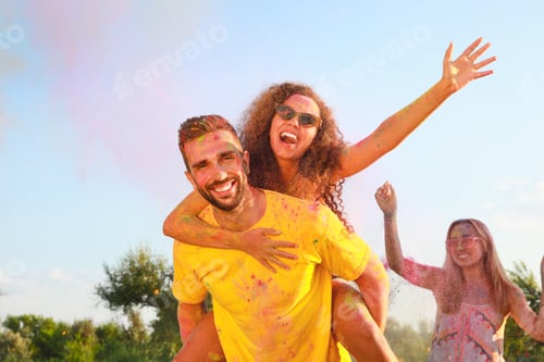 Preview: Happy couple covered with colorful powder dyes outdoors. Holi festival celebration
