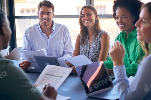 Preview: Multi-Cultural Business Team Meeting Around Office Boardroom Table With Laptops Discussing Documents