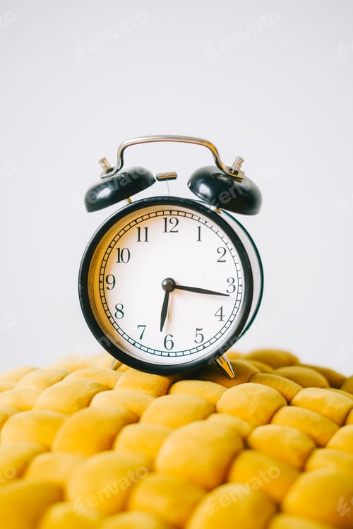 Preview: Black alarm clock on a yellow chair, close up.