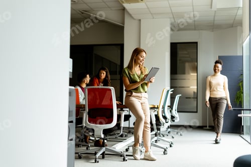 Preview: Young woman standing with digital tablet in front of her team at the office