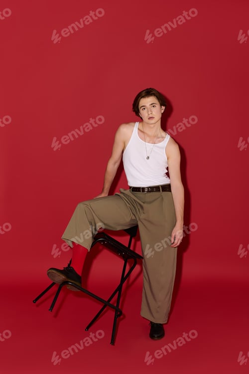 Preview: Young man showcases trendy outfit in stylish pose against vibrant red backdrop