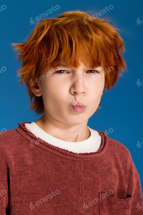 Preview: Fashionable redhead boy poses playfully in vibrant studio setting with unique style