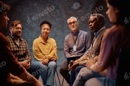 Preview: Senior black man communicating with participants of group therapy at community center.