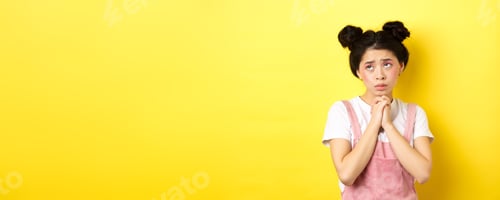 Preview: Sas asian girl holding hands in pray, pleading god, looking up and begging, standing on yellow