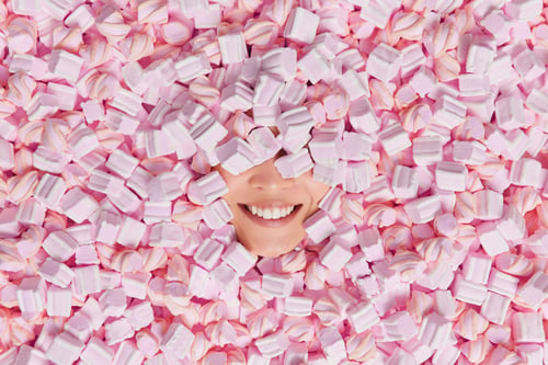 Preview: Positive woman being fully covered with tasty marshmallows smiles toothily. Sweet sticky yumminess a