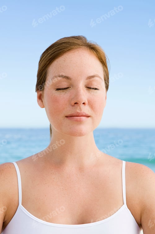 Preview: A young woman seated on the beach in a relaxed pose, with her eyes closed.