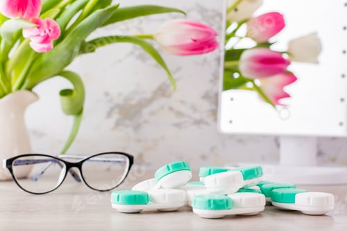 Preview: A pile of containers for lenses and glasses in front of a mirror on the table