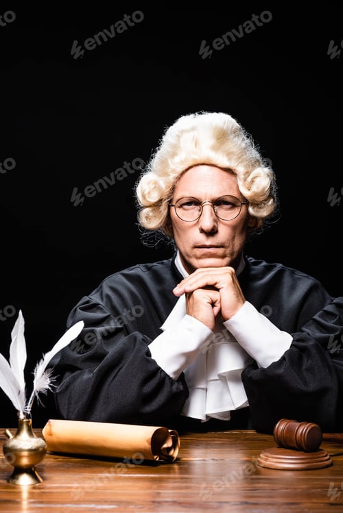 Preview: serious judge in judicial robe and wig looking at camera isolated on black