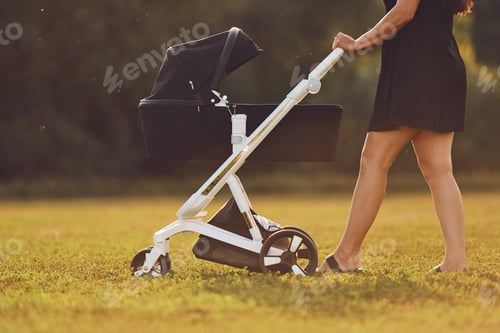 Vorschau: Seitliche Sicht. Mutter mit Kinderwagen geht an sonnigem Tag im Freien auf dem Feld