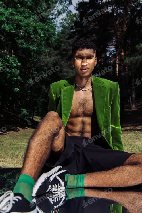 Preview: african american man in green blazer and black shorts sitting with closed eyes in park on reflective