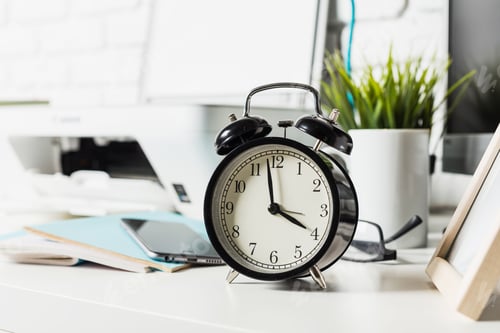 Preview: Classic black alarm clock on a modern workspace with plants and technology in a bright office