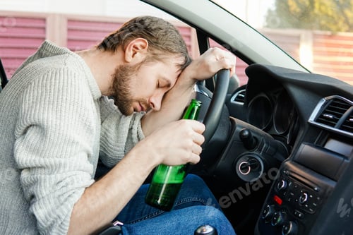 Preview: Young drunk man fall asleep behind the wheel of a car. Male car driver holding bottle of beer.
