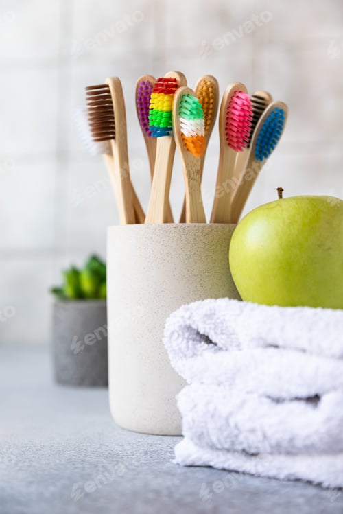 Preview: Bamboo toothbrushes in cup with white cotton towel, plant and green apple.