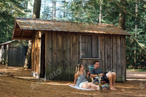 Preview: Young couple relaxing outside hut in forest