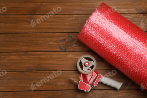 Preview: Bubble wrap roll and tape dispenser on wooden background, flat lay. Space for text