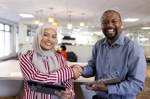Preview: Happy diverse female and male business people shaking hands and looking at camera in office