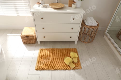 Preview: Stylish orange mat with slippers near chest of drawers in bathroom