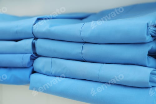 Preview: Light blue medical uniforms on white rack, closeup