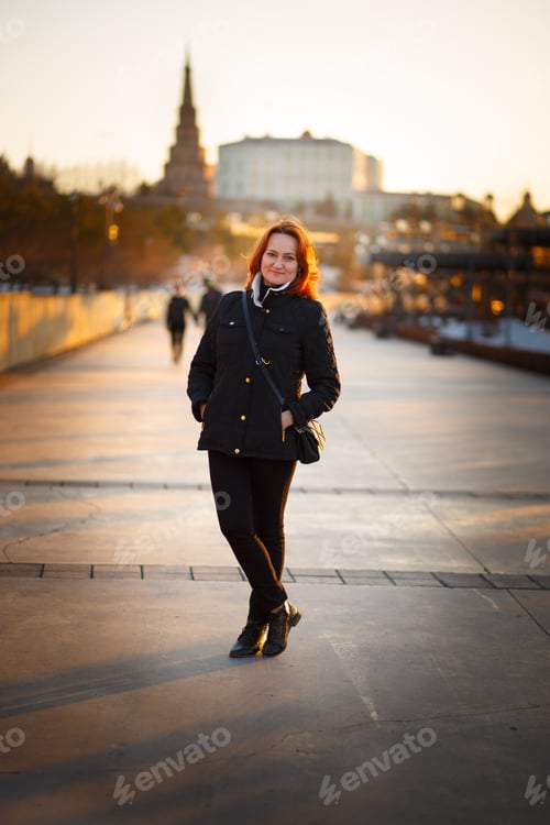 Preview: Young adult lady with red hair walks around the city in spring outdoors