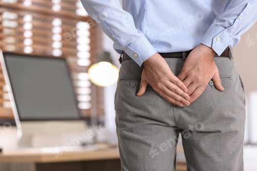 Preview: Man suffering from hemorrhoid in office, closeup