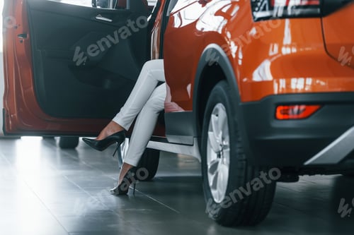 Preview: Sitting in the car. Woman in formal clothes is indoors in the autosalon
