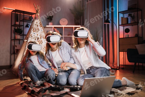 Preview: Caucasian woman and female children sitting outside teepee tent and wearing wireless VR goggles.