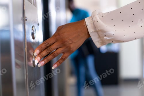 Preview: Cropped hand of young biracial businesswoman pressing elevator button at modern workplace
