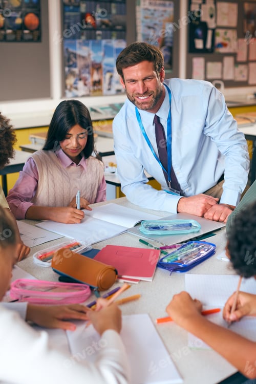 Preview: Male Secondary Or High School Teacher Sitting At Table Working With Students In Classroom