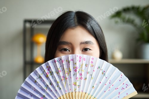 Preview: Portrait of Young Asian Woman Holding Decorative Fan in Modern Office Setting